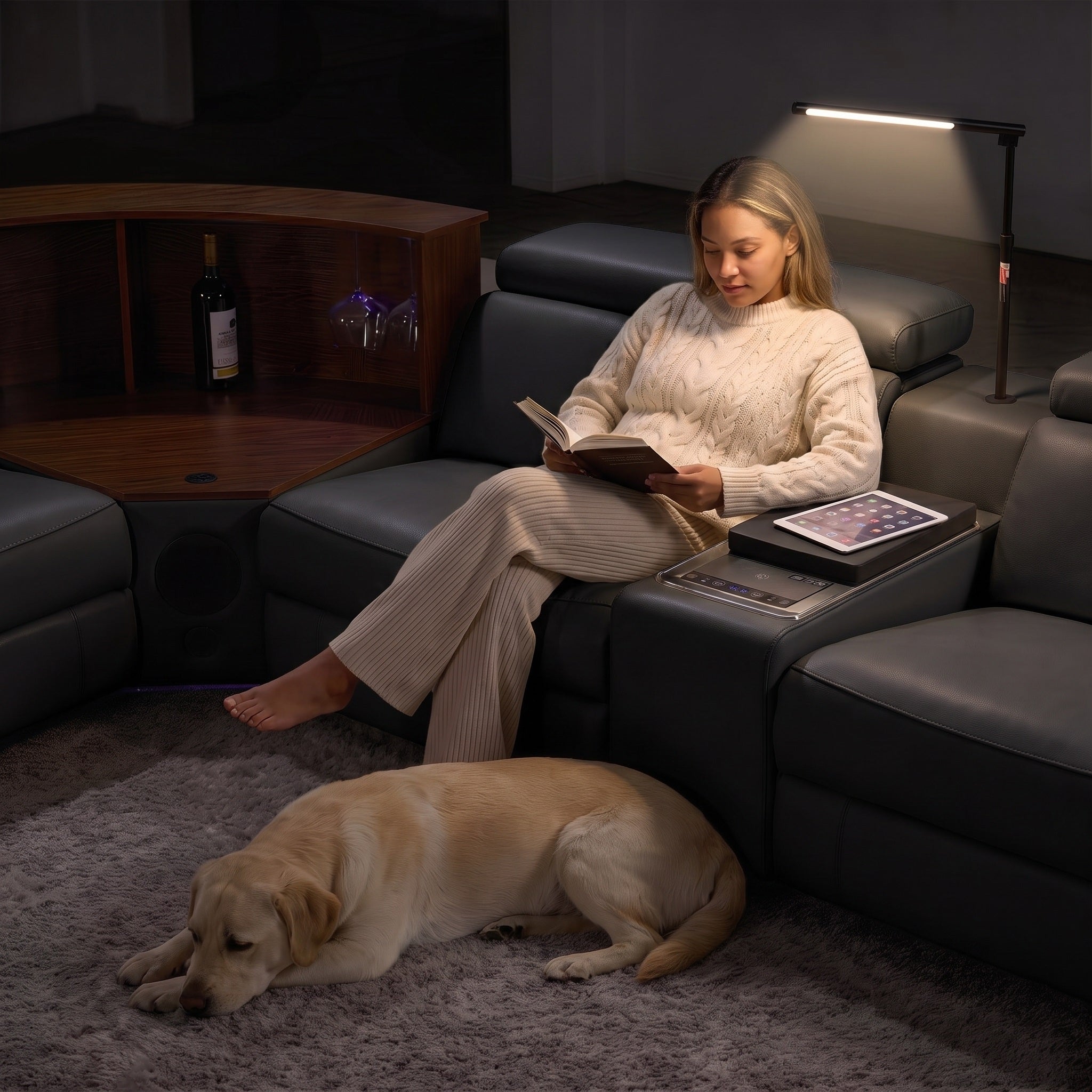 A woman is reading a book while using the lighting fixture on the sofa.